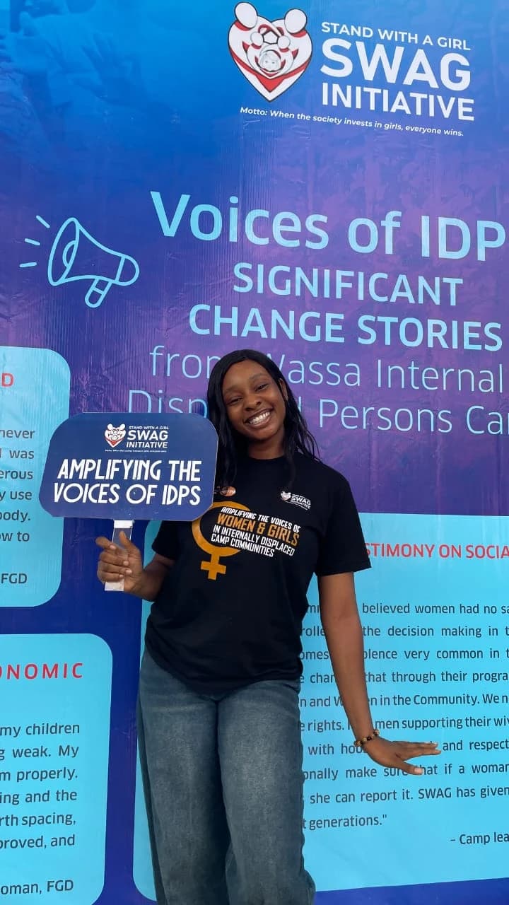 Peace holding an “Amplifying the voices of IDPs” placard in front of the Voices of IDPs exhibition